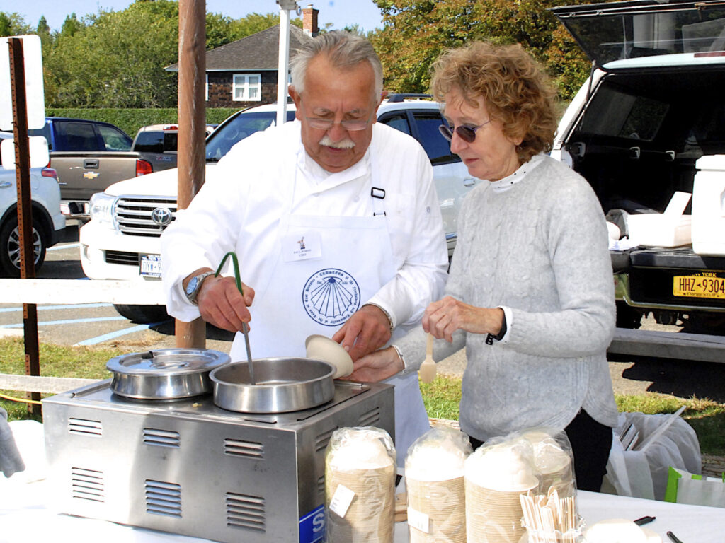 An image of a male chef and a female assistant ladling chowder from a hot tray. 