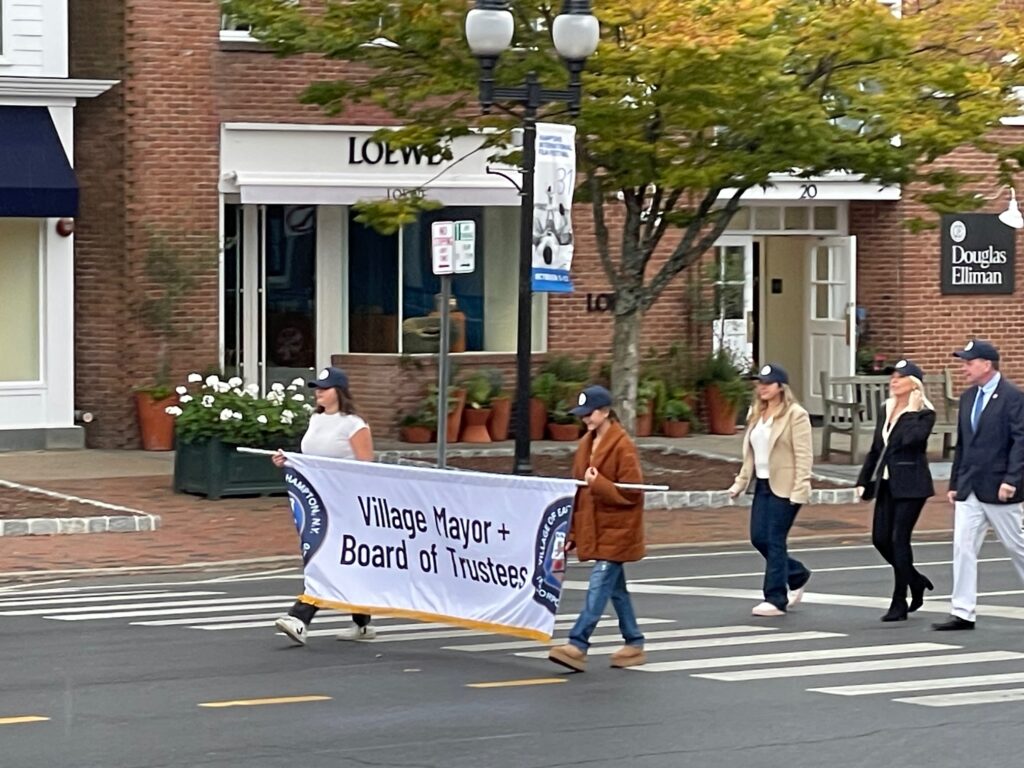Village Mayor & Board of Trustees banner with EH Village Mayor Jerry Larsen and his wife, Lisa Larsen on Main Street in the parade with Village Trustees.