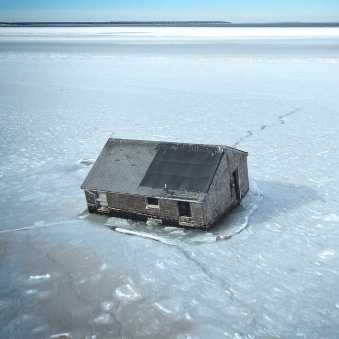 An aerial drone image of the Iconic Hamptons House on Stilts taken by Sky Hampton Aerial. The image shows the cottage, which once stood on stilts, fallen onto the ice of Gardiner's Bay. The Ice holds the structure in place.
