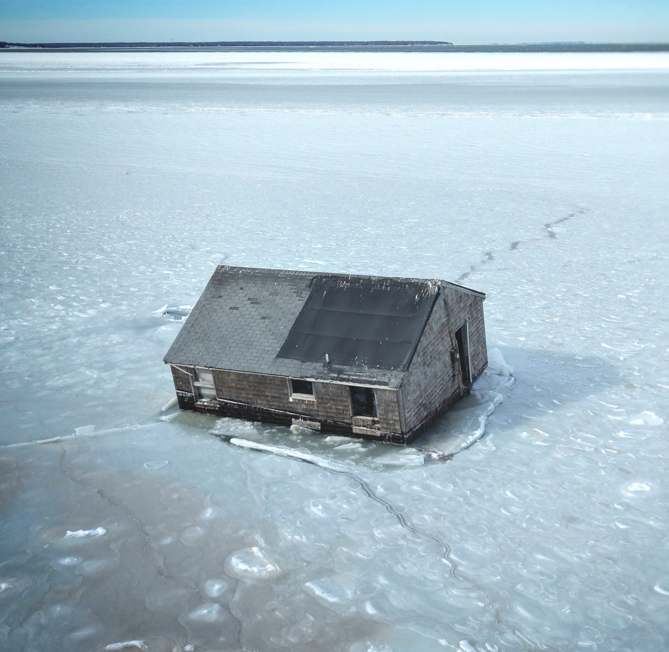 An aerial drone image of the Iconic Hamptons House on Stilts taken by Sky Hampton Aerial. The image shows the cottage, which once stood on stilts, fallen onto the ice of Gardiner's Bay. The Ice holds the structure in place.